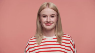 Çizgili tişörtlü neşeli genç bir kadın pembe bir arka planda gülümsüyor, eğlence ve kendine güveni ifade ediyor..