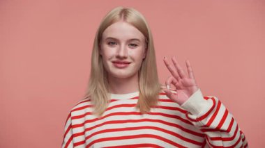 Çizgili tişörtlü kendinden emin genç bir kadın pembe arka plana el kaldırarak onay ya da memnuniyeti sembolize eden pembe arka planda izole edilmiş bir jest yapıyor..