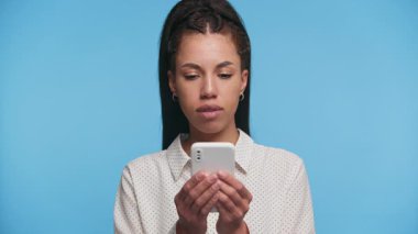 Akıllı telefondan mesaj atarken gülümseyen mutlu genç bir kadın mavi arka plandaki bir mesaja heyecanla tepki veriyor..