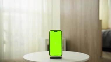 Beyaz yuvarlak bir masa üzerinde boş yeşil ekranlı akıllı telefon, özelleştirilebilir içerik yerleştirme için yakın bir açıdan görüntülenir.