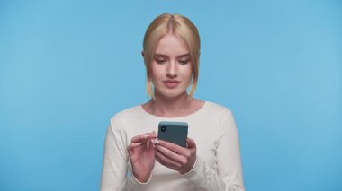 Genç bir kadın beklenmedik bir şey okurken ya da telefonundan mavi bir arka plana karşı endişe verici bir şey okurken ağzını şoka sokuyor..