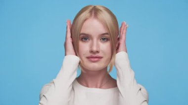 Kadın ellerini mavi arka planda tutuyor, gürültüyü engellediğini ya da sakince dinlemekten kaçındığını gösteriyor..
