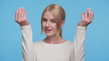 Beyaz bluzlu, kendine güvenen genç bir kadın klasik el hareketi yapıyor. Mavi arka plana karşı nakit ya da ödeme talebi ima ediyor..