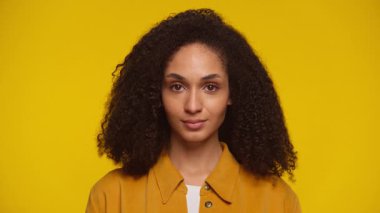 Sarı gömlekli, kendine güvenen genç bir kadının portresi. Saf sarı bir fonda duruyor..