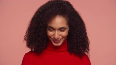 Kırmızı elbiseli neşeli bir kadının portresi kendine güvenen bir gülümsemeyle başını sallıyor, pembe arka planda izole edilmiş bir şekilde uzlaşma ve pozitifliği ifade ediyor..