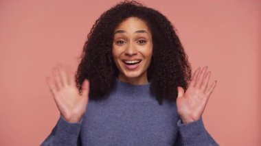 Mavi kazaklı neşeli bir kadın. İki elini de kocaman bir gülümsemeyle sallıyor. Sıcak ve coşkulu bir selamlama jesti yapıyor..