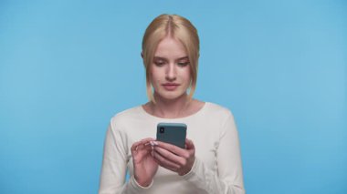 Genç sarışın kadın, mavi arka planda beklenmedik ya da rahatsız edici bir şey okurken şok olmuş görünüyor..