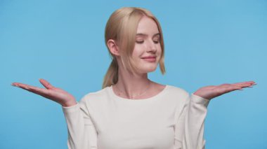 Genç sarışın kadın, iki elini de kaldırırken şaşkın görünüyor. Sanki mavi arka planda iki seçenek varmış gibi..