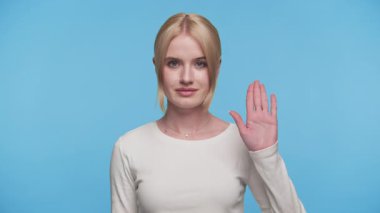 Sakin genç kadın elini kaldırır ince bir dur ya da bekle jesti, düz mavi bir arka plana karşı duran.