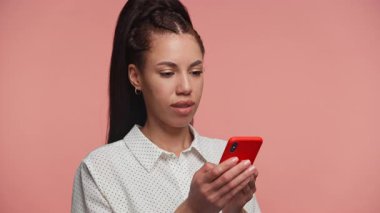 Telli genç bir kadın telefonuyla mesajlaşırken gülümsüyor ve gülüyor. Pembe arka planda neşeli bir anın tadını çıkarıyor..