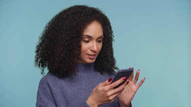 Şaşırmış ve endişeli kıvırcık saçlı genç bir kadın akıllı telefonundan kötü haberler okuyor..