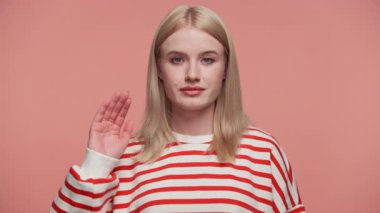 Çizgili tişörtlü genç sarışın kadın elini kaldırarak dur işareti yapıyor. Pembe arka planda uyarı ya da sınır işareti yapıyor..