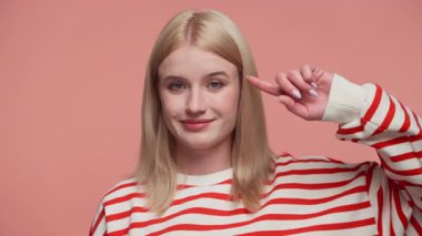 Sırıtarak başını gösteren çizgili tişörtlü sarışın bir kadın. Birinin deli ya da mantıksız davrandığını ima ediyor. Pembe arka planda soyutlanmış..