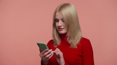 Kırmızı elbiseli sarışın kadın, beklenmedik ya da üzücü haberler gördükten sonra şok olmuş bir şekilde akıllı telefonuna bakıyor..