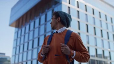 Sırt çantası ve günlük kıyafet giyen öğrenci hızla modern cam binadan geçiyor. Bu da derse geç kaldığını ya da aceleyle gittiğini gösteriyor..