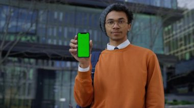 Turuncu kazaklı genç adam yeşil ekranlı akıllı telefonu gösterirken, uygulamayı veya servisi onaylamadığını belirtiyor..