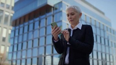 Heyecanlı, gri saçlı, gülümseyen ve yumruğunu sıkan olgun bir kadın akıllı telefondan iyi haberler aldıktan sonra başarıyı kutluyor..