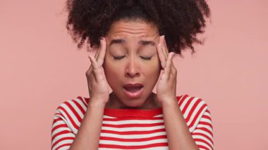 Kıvırcık saçlı ve çizgili gömlekli genç kadın şaşkın ve açık gözlü görünüyor. Üzücü habere şaşırmış ve şok olmuş bir şekilde pembe arka planda izole edilmiş..