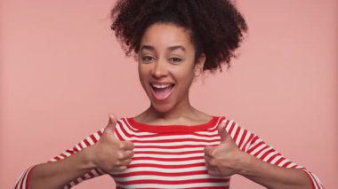 Kırmızı çizgili tişörtlü mutlu genç bir kadın pembe arka planda izole edilmiş onay, pozitiflik ve cesaret veriyor..