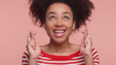 Kırmızı çizgili tişörtlü neşeli genç kadın pembe arka planda izole edilmiş, umut, iyimserlik ve iyi şanslar diliyor..