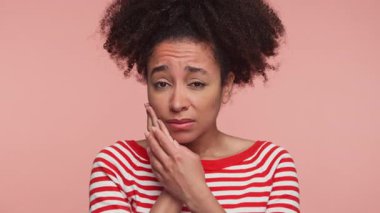 Çizgili gömlekli genç bir kadın, yanak rahatsızlığı çekiyor, diş ağrısı ya da diş sorunları yaşıyor, endişeli bir ifadeyle, pembe arka planda izole edilmiş..