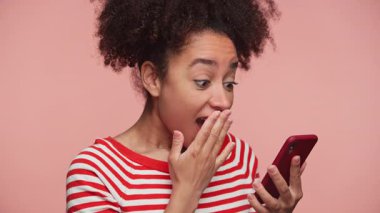 Çizgili tişörtlü heyecanlı genç bir kadın telefonuna bakıyor. Şok olmuş, şaşırmış ve memnun olmuş. Pembe arka planda izole edilmiş özel bir teklif..