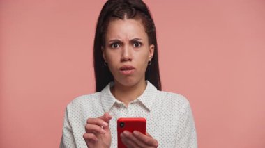 Puantiyeli tişörtlü endişeli genç kadın akıllı telefonu tutuyor ve yüzüne dokunuyor. Beklenmedik ya da rahatsız edici mesaja tepki veriyor..