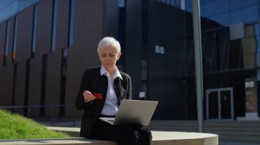 Üst düzey kadın dışarıda dizüstü bilgisayar kullanırken stresli görünüyor, online ödeme veya kredi kartı girişi sırasında bir soruna tepki veriyor.