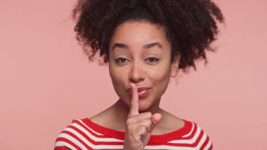 Kırmızı çizgili tişörtlü, gülümseyen genç bir kadın parmaklarıyla şşşş hareketi yapar..