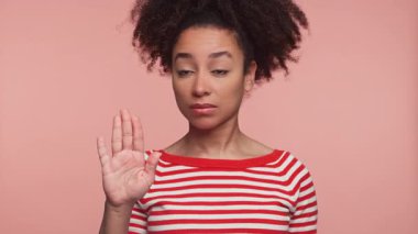 Kırmızı çizgili tişörtlü bir kadın ciddi bir ifadeyle elini kaldırır. Reddedilme, inkar sinyali verir ya da birinden durmasını ister. Pembe arka planda izole bir şekilde..