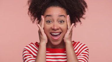 Çizgili tişörtlü neşeli kadın pembe arka planda geniş gözleri ve elleri olan heyecan ifade ediyor.