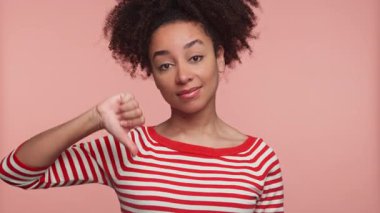 Onaylamadığını ifade eden kendinden emin genç bir kadın. Pembe arka plana karşı olumsuz geri bildirim ya da tatminsizliği simgeliyor..