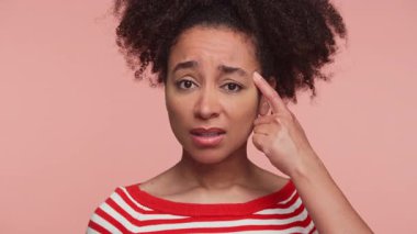 Kafasını işaret eden kafası karışmış genç bir kadın, pembe arka planda inançsızlığı ya da akıl sağlığını sorgulamayı öneriyor..