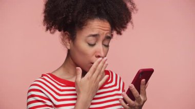 Genç kadın şok olmuş görünüyor ve pembe arka planda rahatsız edici ya da üzücü bir şey okurken ağzını kapatıyor..