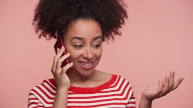 Genç bir kadın neşeli bir telefon görüşmesi yapıyor. Elleriyle gülümsüyor ve pembe bir arka plana el sallıyor..