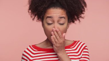 Çizgili gömlekli genç bir kadın, beklenmedik olumsuz haberlere tepki veriyor. Geniş gözlü ve ağzı açık, pembe bir arka planı var..