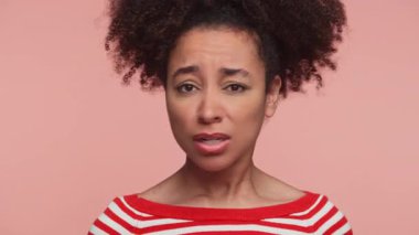 Hüsrana uğramış, çizgili tişörtlü genç bir kadın onaylanmayan yüz ifadesiyle kafasını sallıyor, yumuşak pembe bir arka plana çekiliyor..