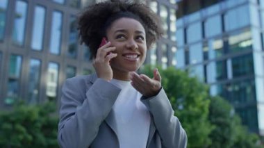 Şehirde yürüyen gülümseyen bir kadın, şehir merkezinde spor ceket giyerken canlı bir telefon görüşmesi yapıyor..
