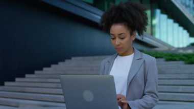 Profesyonel bir kadın şehrin merdivenlerinde dizüstü bilgisayarla oturup uzaktan kumanda sırasında bir karar vermek için düşünceli bir duraklama yapıyor..