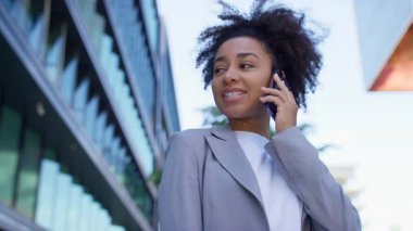 Kendine güveni tam genç bir kadın, şehir merkezindeki modern bir ofis binasının dışında telefonla konuşurken gülümsüyor..