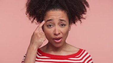 Kırmızı çizgili tişörtlü, hayal kırıklığına uğramış genç bir kadın pembe arka planda inançsızlık, kafa karışıklığı ya da sorgulama ifade ediyor..