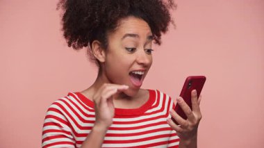 Çizgili tişörtlü neşeli genç bir kadın. Yumruk pompasıyla tezahürat yapıyor. Akıllı telefonundan harika haberler okuyor..