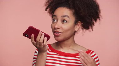 Kırmızı çizgili gömlekli genç bir kadın akıllı telefonuna konuşuyor, bir sesli mesaj kaydediyor ya da pembe arka planda ses asistanı kullanıyor..