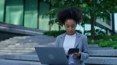 Odaklanmış kadın şehir basamaklarında hesap makinesi ve dizüstü bilgisayar kullanarak oturur, modern bir iş ortamında finans veya açık hava bütçesi yönetir..