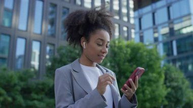 Spor ceketli, akıllı telefon kullanırken, kulaklık takıp, ekrana odaklanmış, bağlantıyı ve çoklu görevi temsil eden kendine güvenen bir kadın..