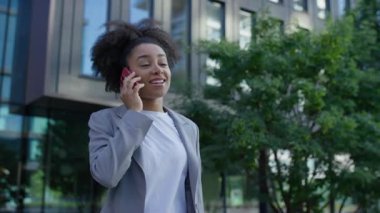 Gülümseyen genç profesyonel kadın modern ofis binalarının dışında telefon görüşmesi yapıyor. Güven, iletişim ve başarıyı ifade ediyor..