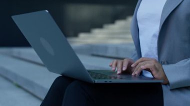 Dışarıda dizüstü bilgisayar kullanan bir iş kadınının detaylı görüntüsü, dokunmatik dokunmatik ekranda parmaklarıyla kayıyor, teknolojiyi, hareketliliği ve verimliliği simgeliyor..
