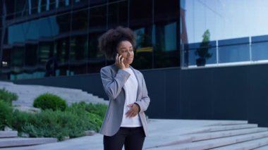 Modern ofis binalarının dışında duran, cep telefonuyla gülümseyen ve konuşan profesyonel kadın iletişimi, başarıyı ve bağlantıyı simgeliyor..