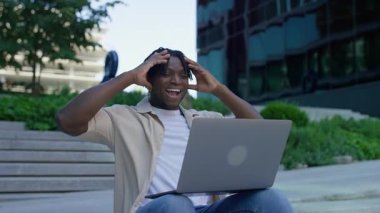 Dışarıdaki merdivenlerde dizüstü bilgisayarla oturan neşeli genç adam, şaşırtıcı olumlu haberler aldıktan sonra şok ve heyecan ifade ediyor..