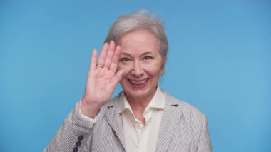 Gülümseyen yaşlı kadın el sallayarak selamlıyor, dostluk, iletişim ya da hoş geldin işareti yapıyor..